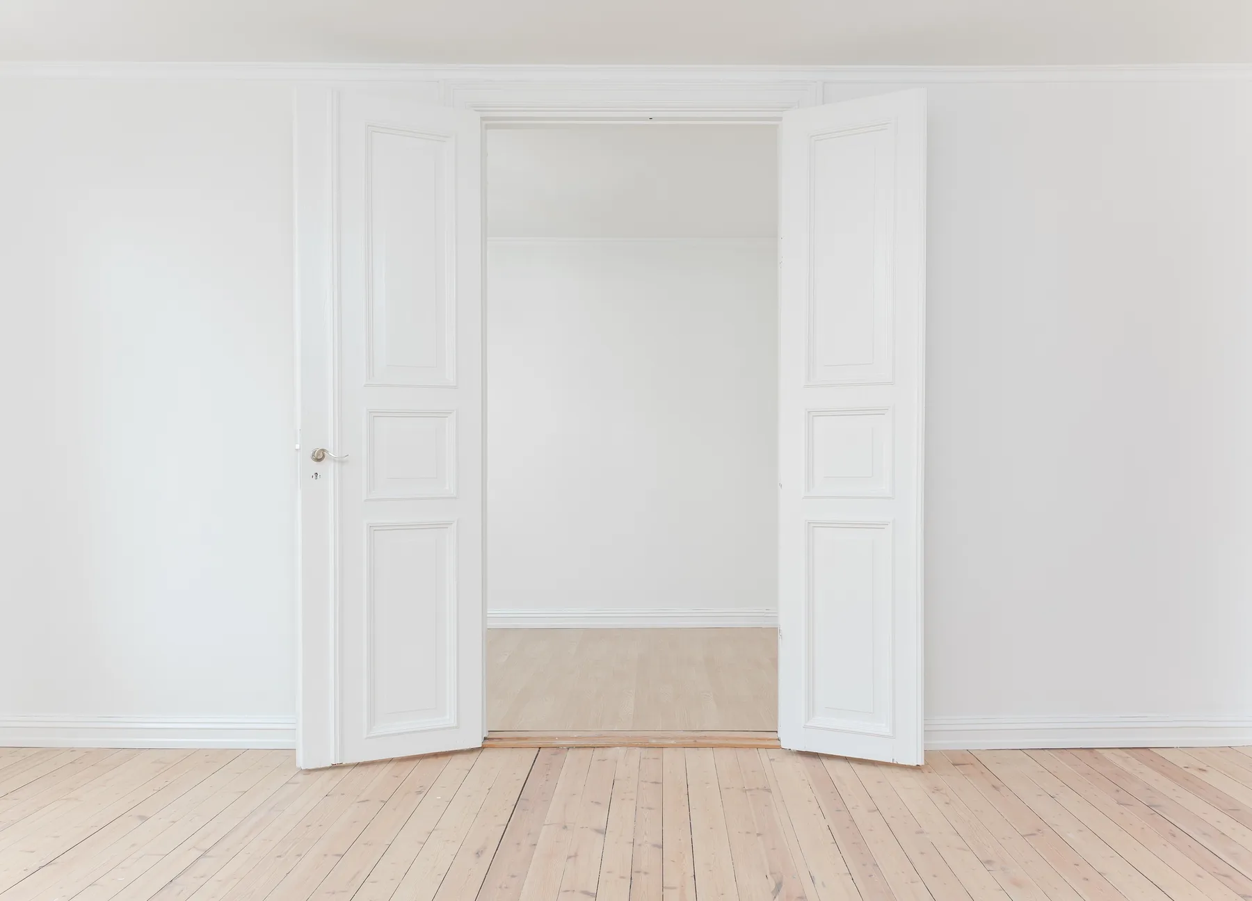 Open white double doors leading into a bright, empty room with a pale wooden floor